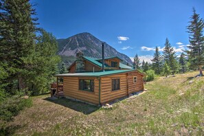 Eine Blockhütte mit einem grünen Dach, umgeben von Bäumen und einem Berg im Hintergrund.