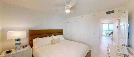 A hotel room with a bed, nightstand, lamp, ceiling fan, and a bathroom mirror.