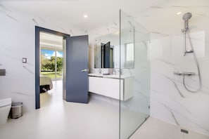 A modern bathroom with a glass shower enclosure, a white marble wall, and a large mirror.