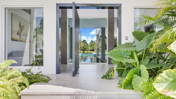 A modern house with a glass door leading to a pool, surrounded by lush greenery. - Ultra Modern Villa with Chef & Maid (Punta Cana)