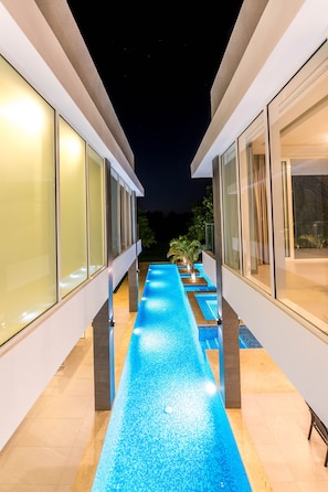 A modern building with a long, narrow pool with blue lighting, large glass windows, and a well-lit exterior.