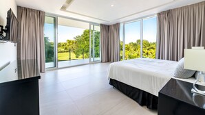 A modern bedroom with a large bed, a desk, and a view of greenery through floor-to-ceiling windows. - Ultra Modern Villa with Chef & Maid (Punta Cana)