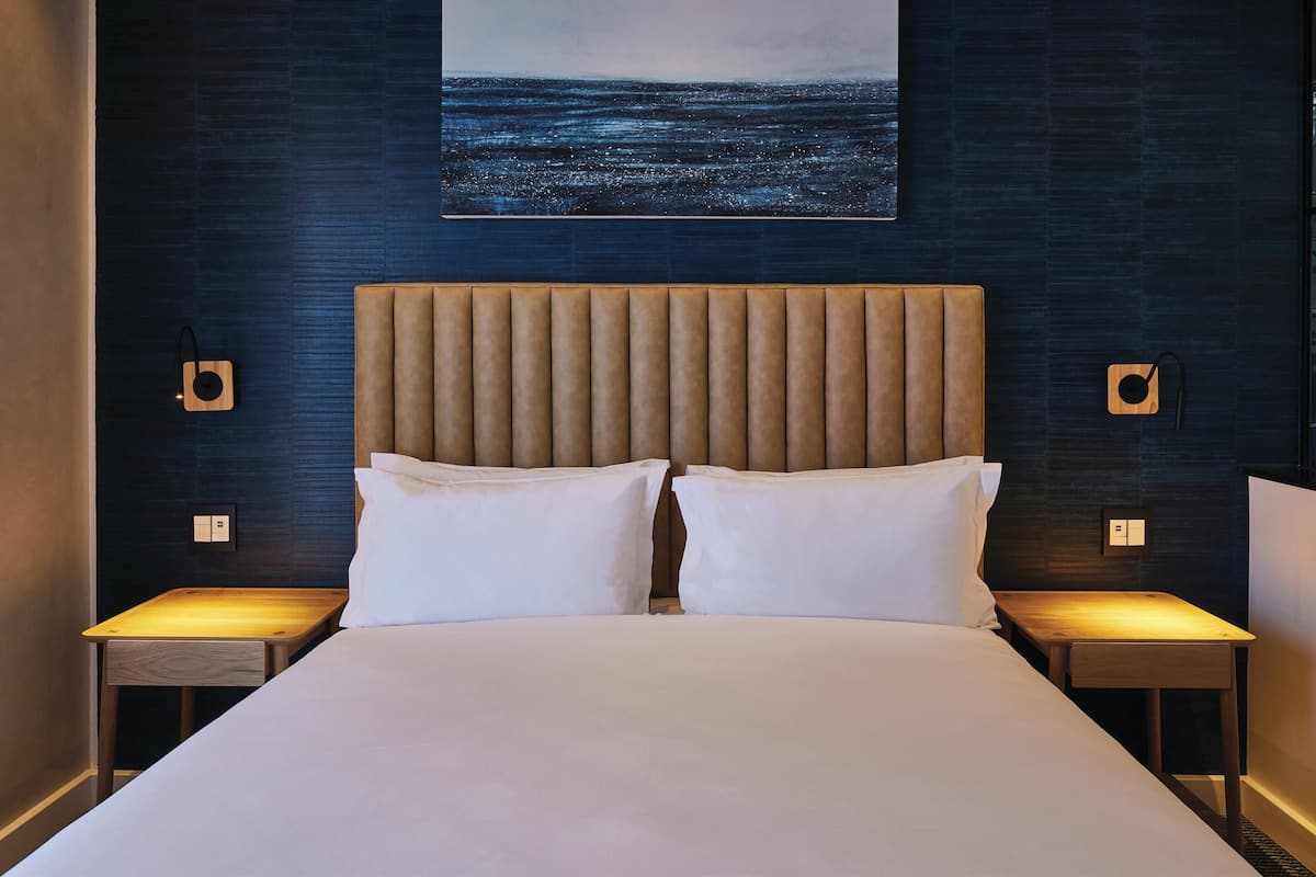 Een moderne hotelkamer met een groot bed, twee nachtkastjes, een kunstwerk aan de muur en uitzicht op zee.