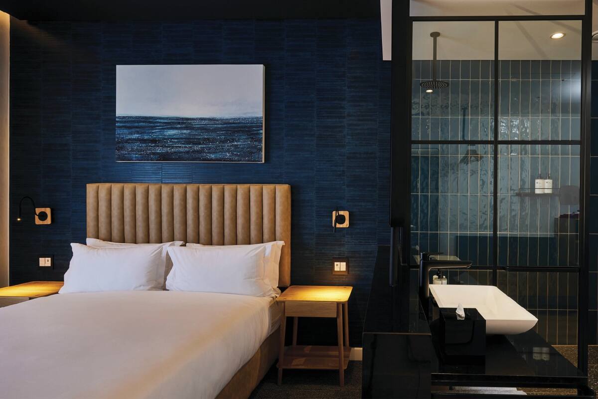 Een moderne hotelkamer met een bed, nachtkastjes, een glazen douchecabine en een groot raam.