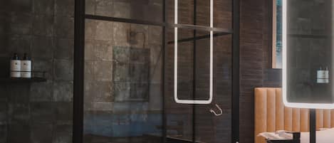 Un baño moderno con cabina de ducha de vidrio, un espejo grande, un lavabo blanco y un mueble de tocador de madera.