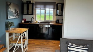 A modern kitchen with black cabinets, a wooden countertop, and a window overlooking a green field.
