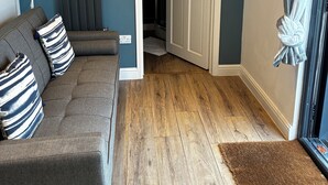 A living room with a dark blue wall, a grey sofa with striped pillows, a white floor lamp, and a wooden floor.