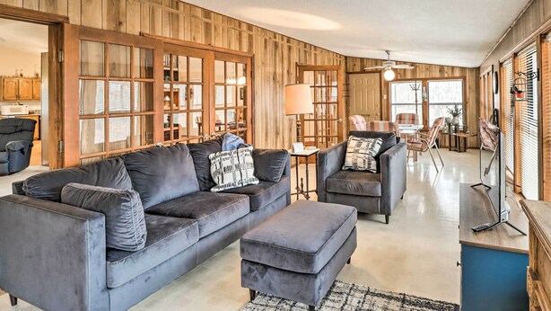 Een ruime woonkamer met een donkergrijze zithoek, een bijpassend voetenbankje en een wand bekleed met hout.