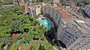 A high-rise hotel with multiple balconies, a swimming pool, and lush greenery surrounding the property.