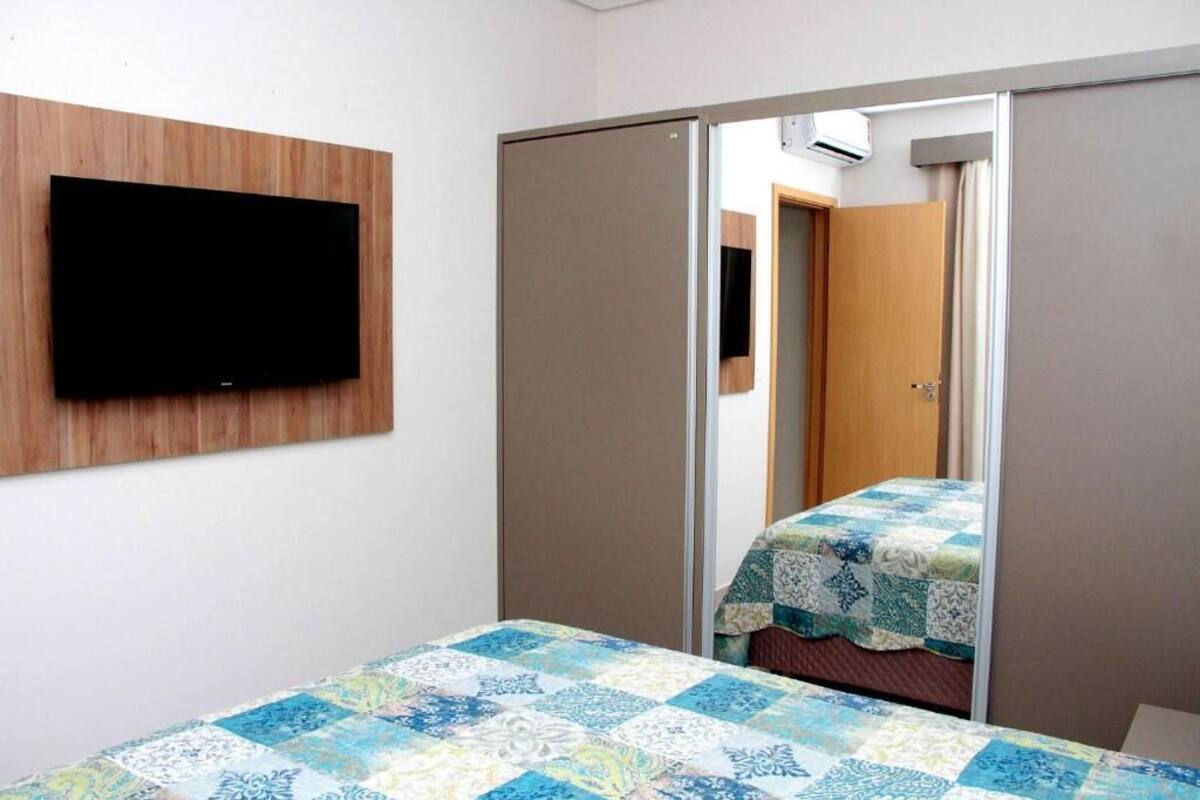 A bedroom with a bed, a television mounted on the wall, and a wardrobe with a mirror.