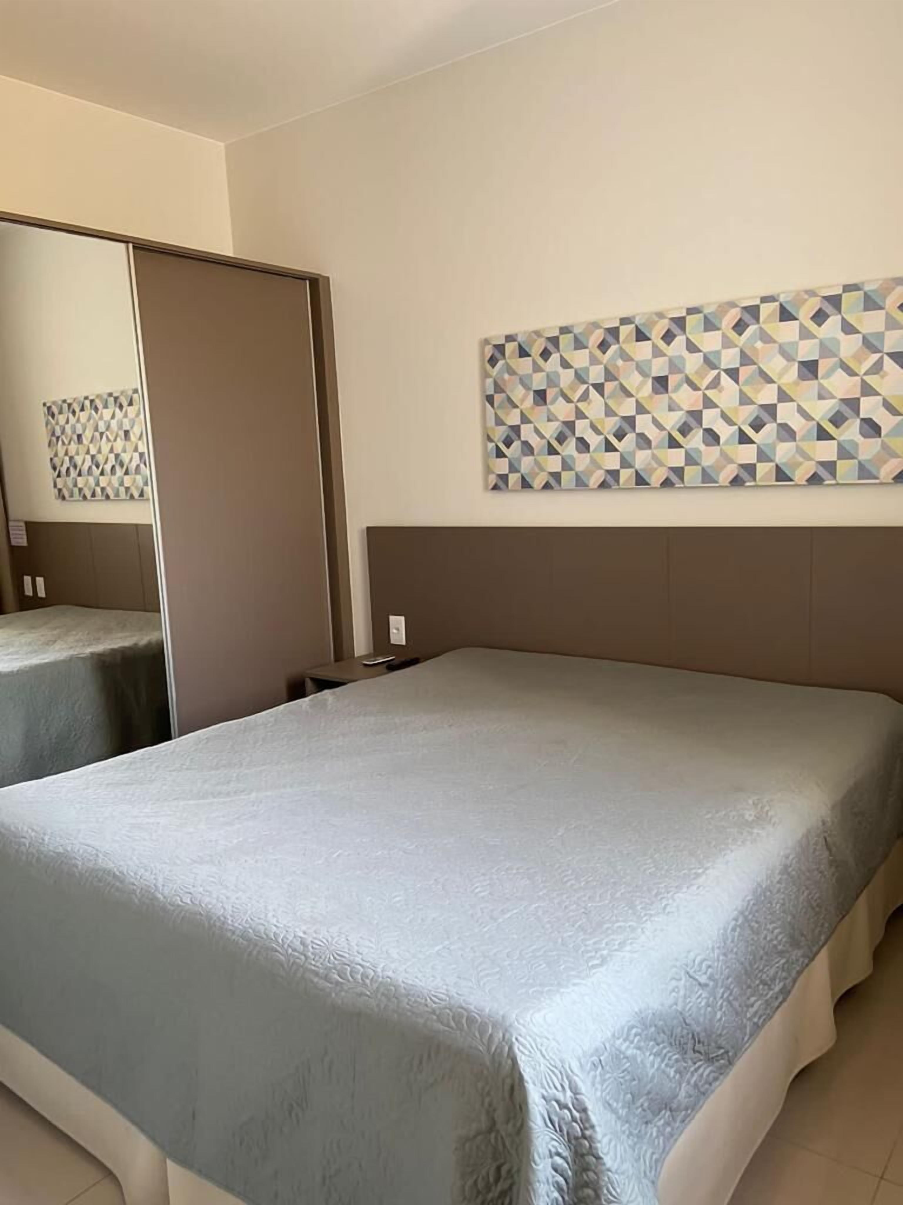 Habitació d'hotel amb un llit gran, un mirall i una obra d'art mural amb un dibuix geomètric.