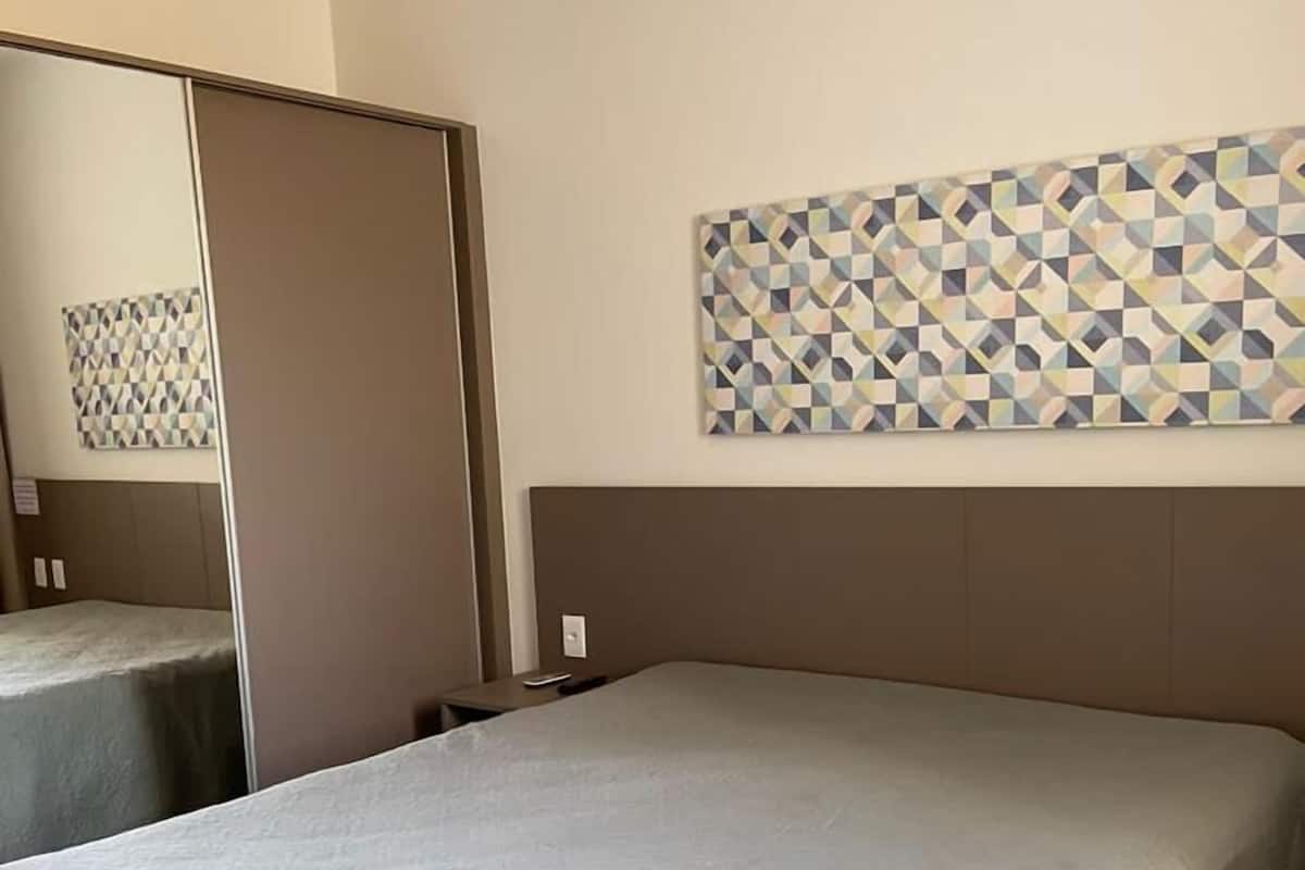 Une chambre d’hôtel avec un grand lit, un miroir et une œuvre d’art murale aux motifs géométriques.