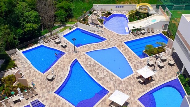 Un espace piscine sur le toit, comprenant plusieurs piscines, des chaises longues et un espace de jeux pour enfants.