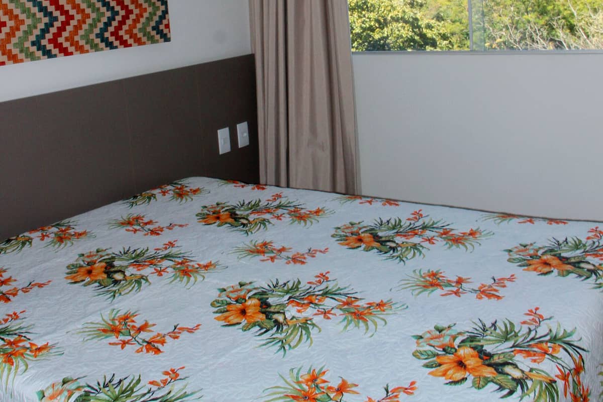 A hotel room with a bed, a window with curtains, a wall with a patterned artwork, and a view of buildings and hills outside.