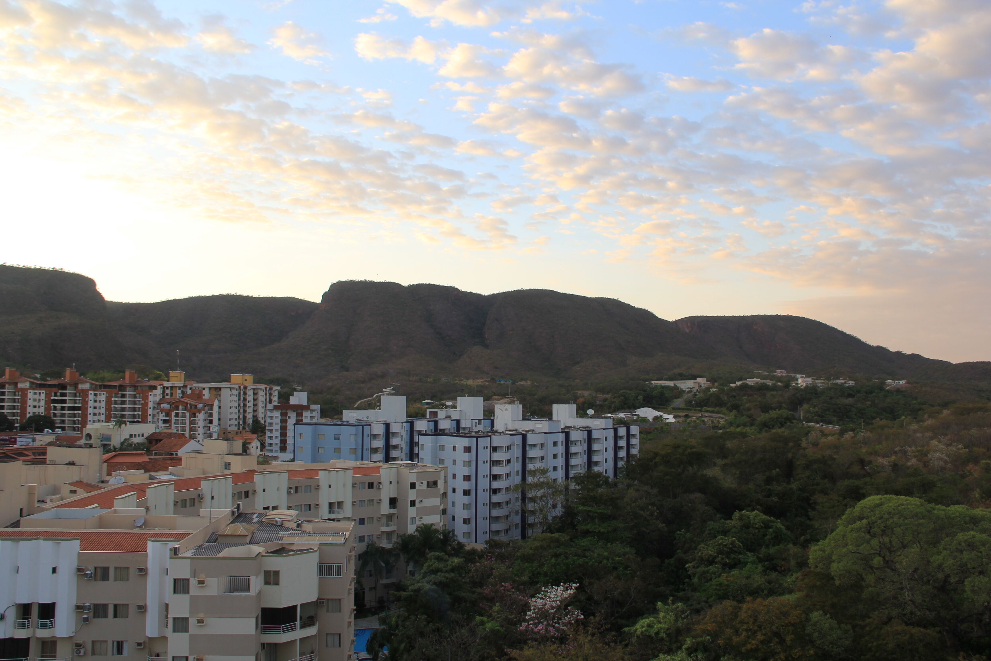 A residential area with multi-story buildings, surrounded by greenery and hills in the background.
