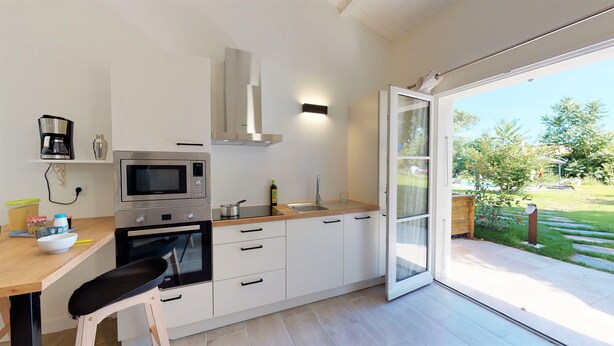 A modern kitchen with a built-in oven, microwave, and a large window opening to a garden. - 2 gites in a green setting (Sainte-Marie-de-Ré)