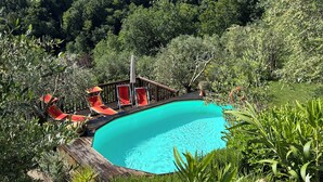 Piscina cercada por vegetação exuberante e um deck de madeira com espreguiçadeiras.