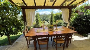 Mesa de madeira com quatro cadeiras, um castiçal e um jogo de mesa com um cartão de identificação em uma área externa coberta.
