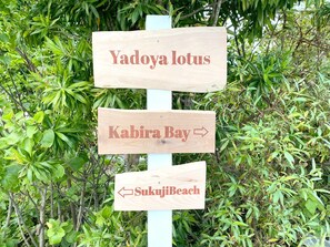 A wooden signpost with directions to Yadoya Lotus, Kabira Bay, and Sukujii Beach.