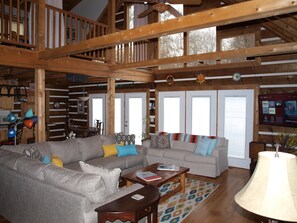 A spacious living room with two sofas, a wooden ceiling, and a TV mounted on the wall.