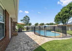 Un jardin avec une piscine, une terrasse dotée d’une table et de chaises, et un espace clôturé.
