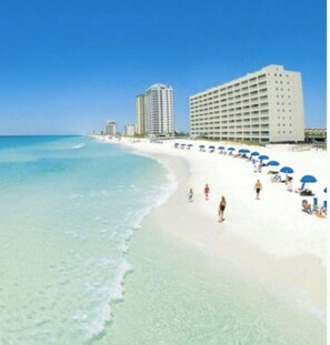 A beach with a row of blue umbrellas and a large hotel building.