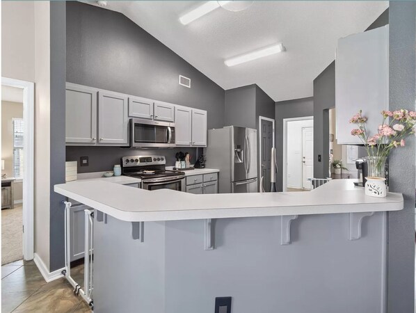 A modern kitchen with grey cabinets, stainless steel appliances, and a white island.
