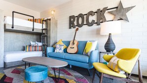 A modern living room with a bunk bed, a blue sofa, a yellow armchair, a guitar, and a 'ROCK' sign on the wall. - Egyptian Motor Hotel, Bw Signature Collection (Phoenix)