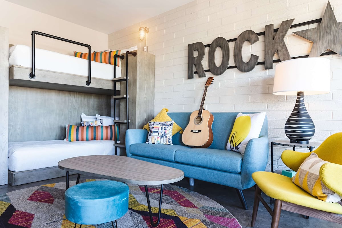 Una sala de estar moderna con una cama litera, un sofá azul, un sillón amarillo, una guitarra y un letrero en la pared que dice 'ROCK'.