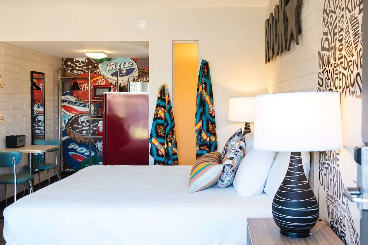 Habitación de hotel con cama, escritorio, silla, refrigerador y una pared decorada con varios adornos.