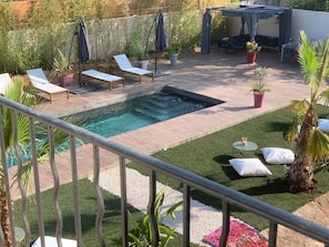 A backyard with a swimming pool, lounge chairs, a covered seating area, and potted plants.