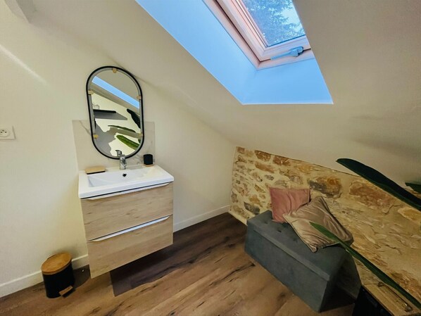 Una camera da letto con un lucernario, pavimento in legno, testiera in pietra e comodino con lampada.