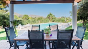 Un espacio de estar al aire libre cubierto con vista a la piscina, que incluye una mesa y sillas, y una pérgola encima.