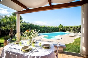 Un área de comedor al aire libre con piscina y sillas de descanso.