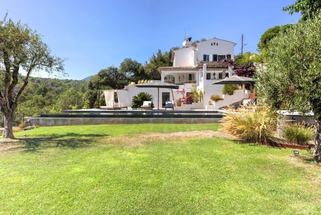 Eine weiße Villa mit einer geräumigen Terrasse, umgeben von üppigem Grün und Blick auf die Hügel.