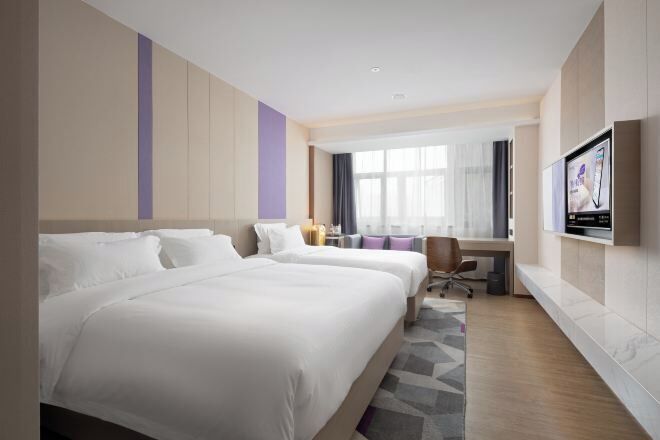 A hotel room with two beds, a desk, a chair, and a TV on the wall.
