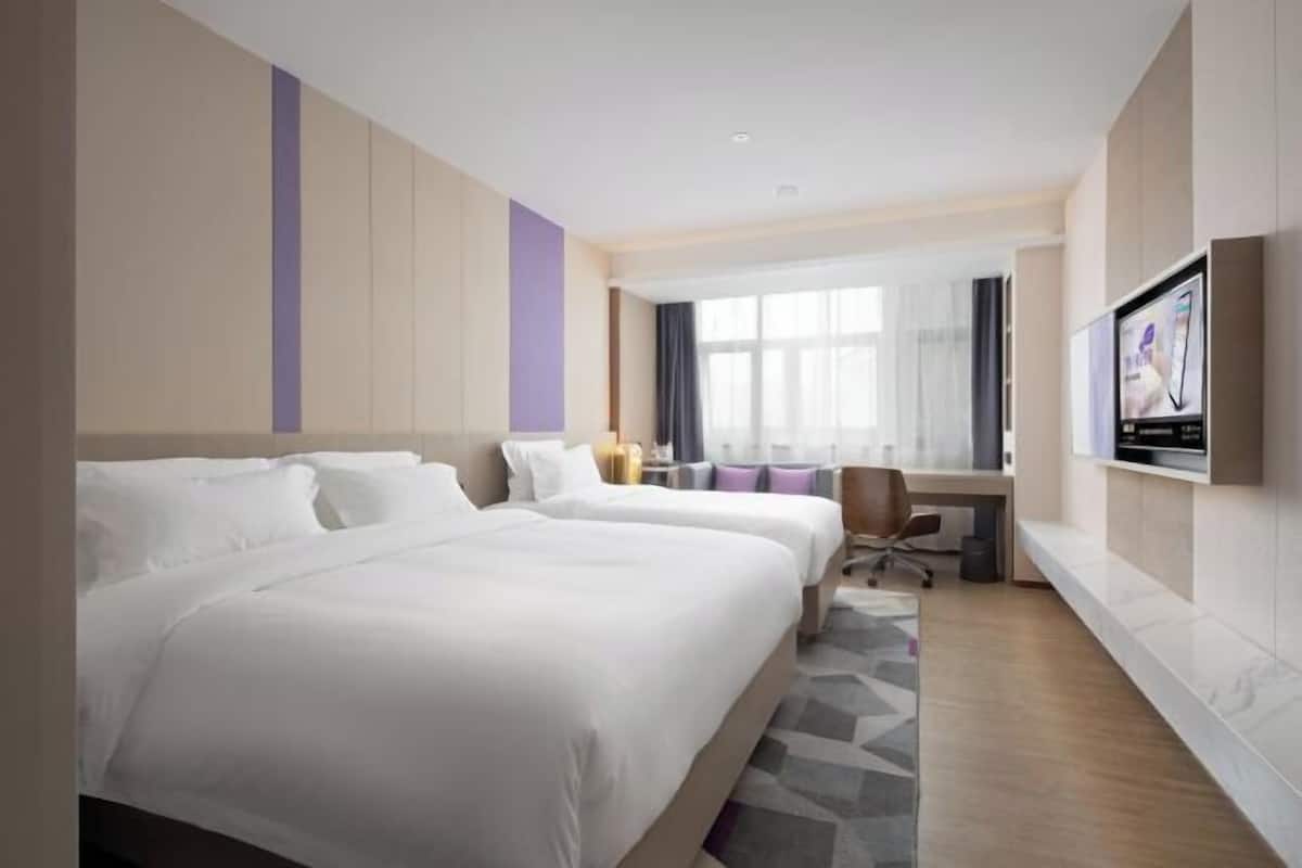 A hotel room with two beds, a desk, a chair, and a TV on the wall.