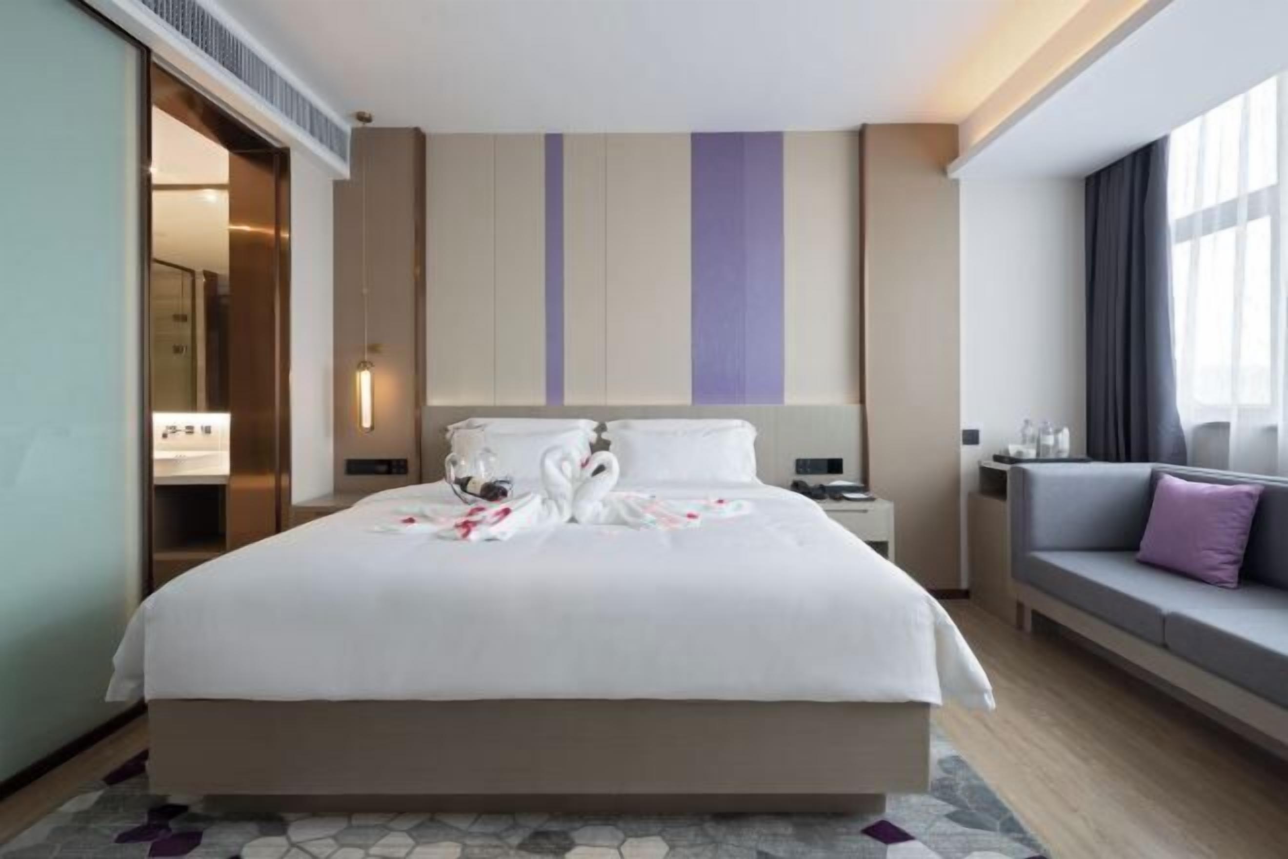 A hotel room with a large bed, a sofa, a nightstand, and a window with curtains.