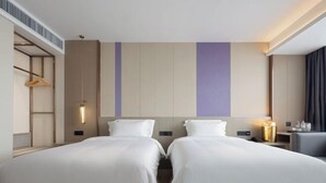 Camera d'albergo con due letti, un comodino con lampada, un armadio e un appendiabiti.