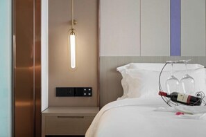 Ein Hotelzimmer mit Bett, Nachttisch, Wandleuchte und einer Weinflasche auf dem Bett.