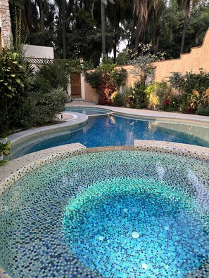 Una piscina de borde infinito con mosaicos y un borde de piedra, rodeada de exuberante follaje y palmeras.