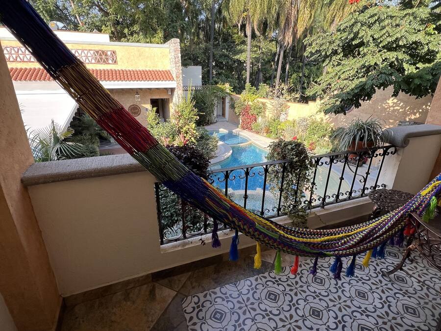 Un balcón con una hamaca, una piscina y follaje circundante.