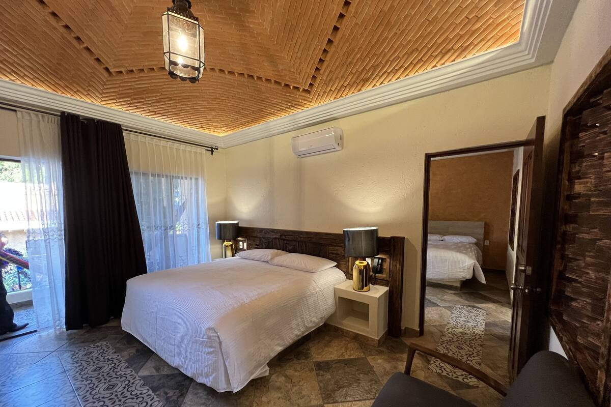 A hotel room with a large bed, bedside lamps, a mirror, and a ceiling with a wooden design.