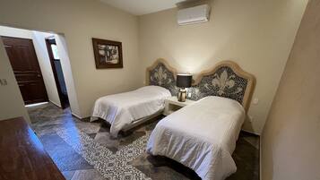 A hotel room with two beds, a nightstand with a lamp, a wall-mounted air conditioner, and a patterned rug.