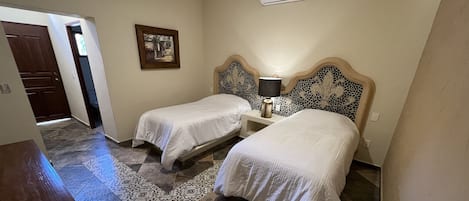 Habitación de hotel con dos camas, una mesita de noche con lámpara, aire acondicionado de pared y una alfombra estampada.