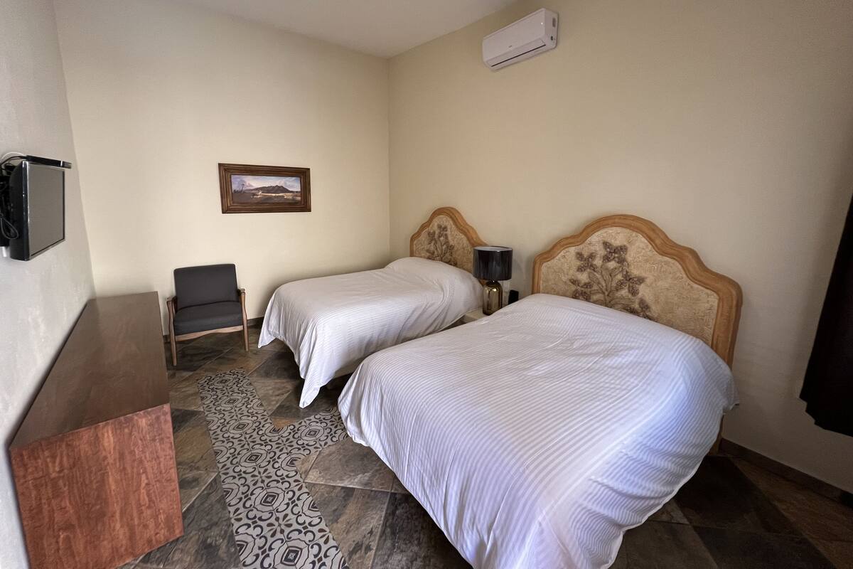 A hotel room with two beds, a desk, a chair, an air conditioner, and a framed picture on the wall.
