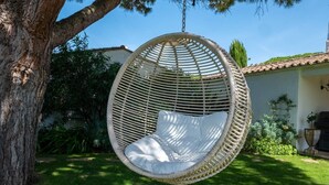 Un fauteuil suspendu en osier, agrémenté d’un coussin, dans un jardin.