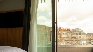 A hotel room with a bed, a window with curtains, and a view of buildings and parked cars outside. - Radisson Hotel Liege City Centre (Liege)