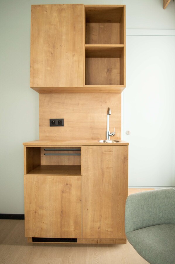 A wooden kitchenette with a sink, a small countertop, and a cabinet with two shelves.