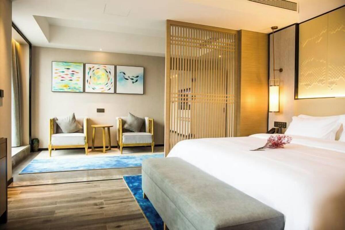 Habitación de hotel con una cama grande, una zona de estar con dos sillones, una mesita y obras de arte en la pared.